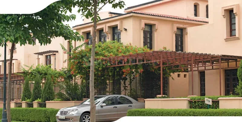 Jaypee Greens Villas — Front view of an Indian residential villa with a parked car, lush greenery, and a pergola