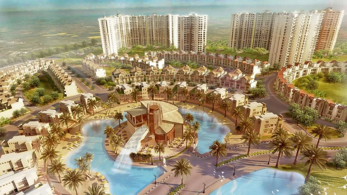 Supertech Holiday Village — An aerial render of a large residential project with villas, high-rise buildings, an artificial lake, and palm trees.