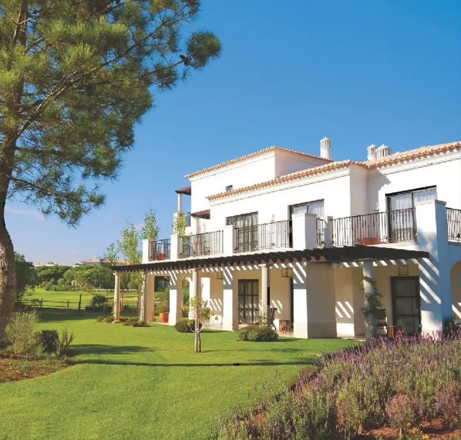 Jaypee Villa Expanza Green Crest Homes — A white Mediterranean-style villa with a green lawn, balcony, and covered patio area under a bright blue sky.
