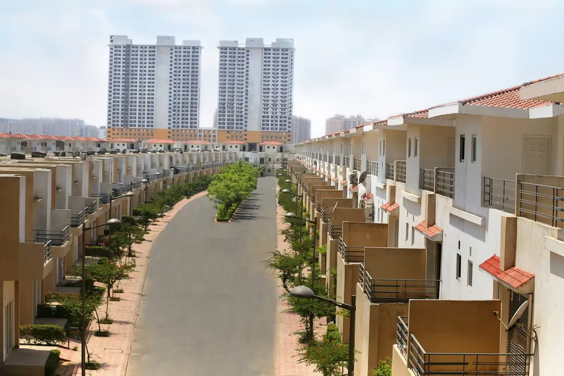 Paramount Golfforeste Villas — A wide view of a residential street lined with villas, with two tall apartment buildings in the background.