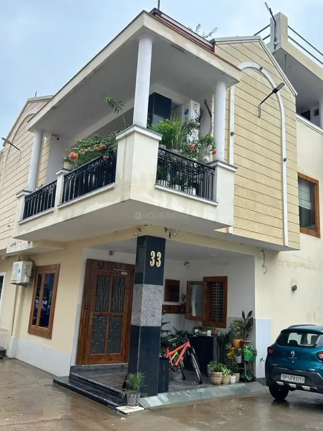 Arsh Green Villa 2 — Front view of a residential villa with a balcony adorned with potted plants and a car parked outside.