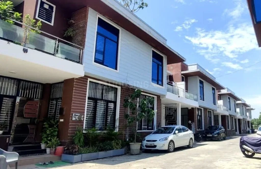 Shivi Paradise Green Villa 2 — Row of modern two-story residential villas with blue-tinted windows, brown and light-colored facades, and parked cars outside.